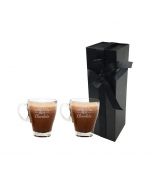 Personalised glass cup engraved with any names above the words 'hot chocolate', this picture shows two cups standing in front of a tall and thin black box with a white background